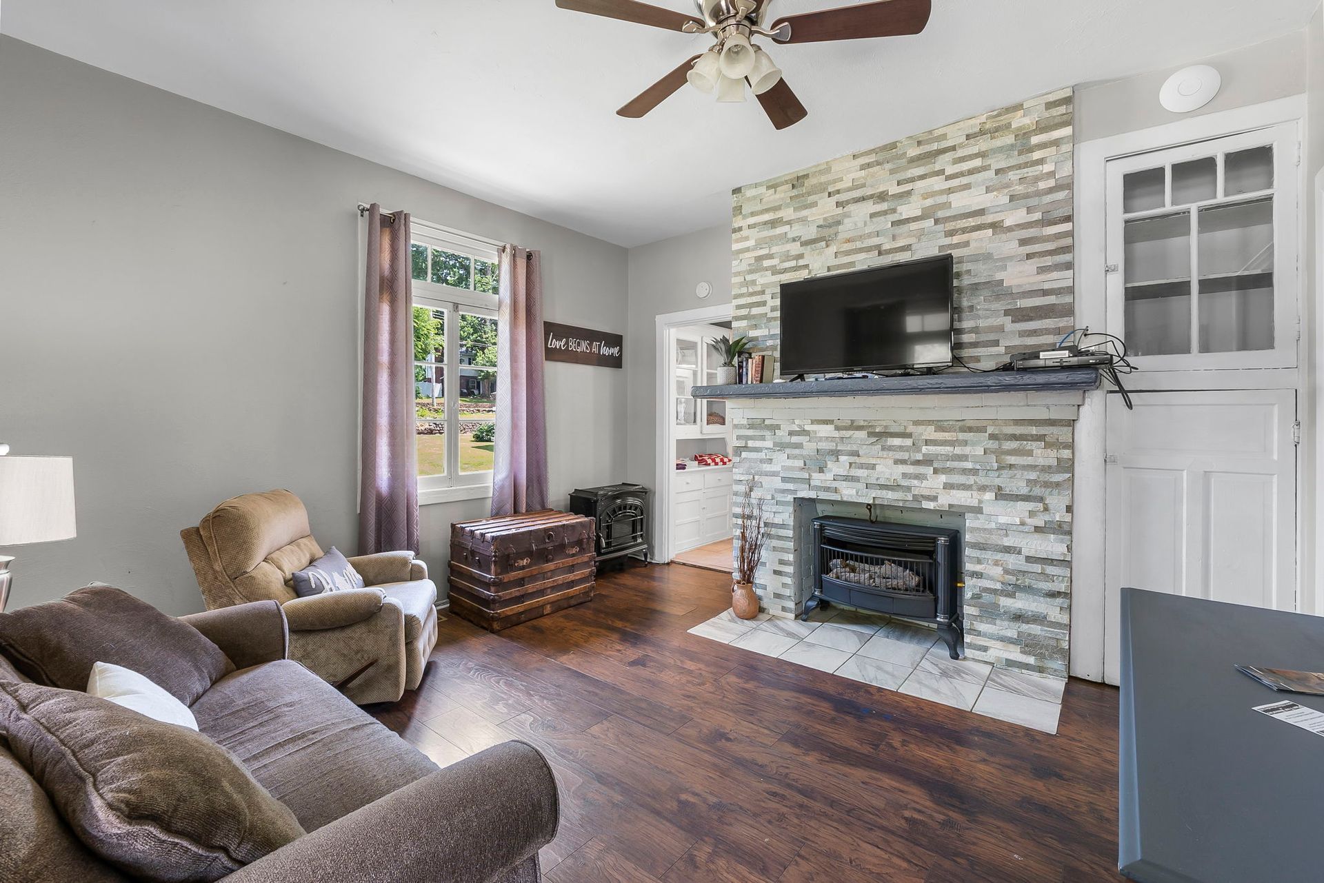 A living room with a stone fireplace and a flat screen tv.