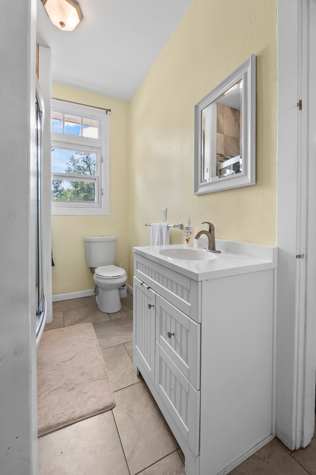 a bathroom with a toilet , sink , mirror and window .