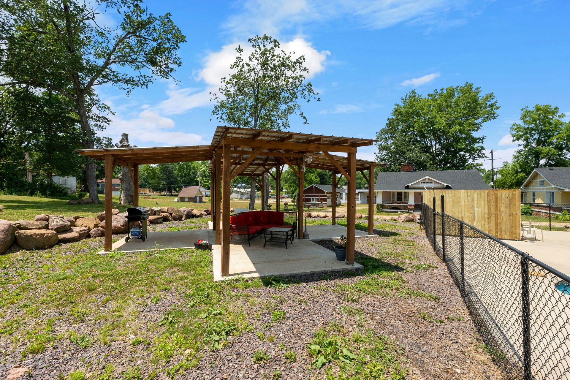 A pergola with a red couch and a grill in the backyard of a house.