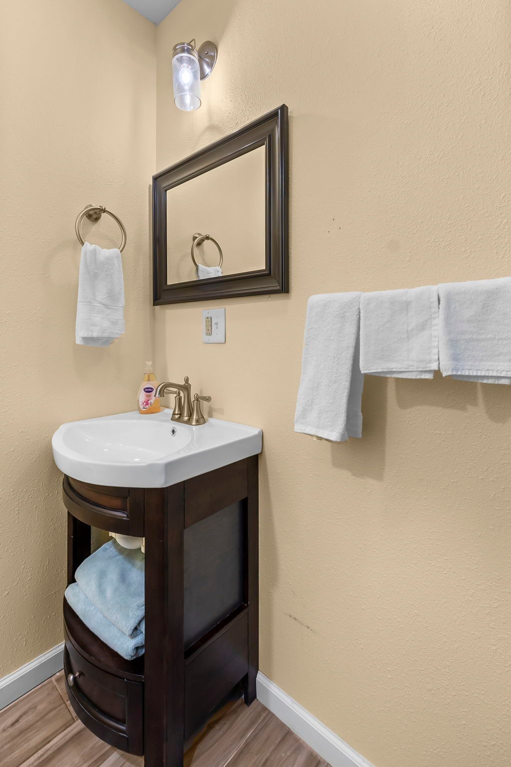 A bathroom with a sink , mirror , and towels hanging on the wall.