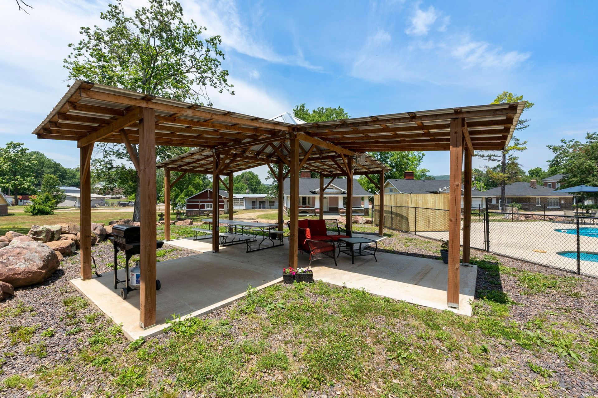 A wooden gazebo with a grill and picnic tables in a park.