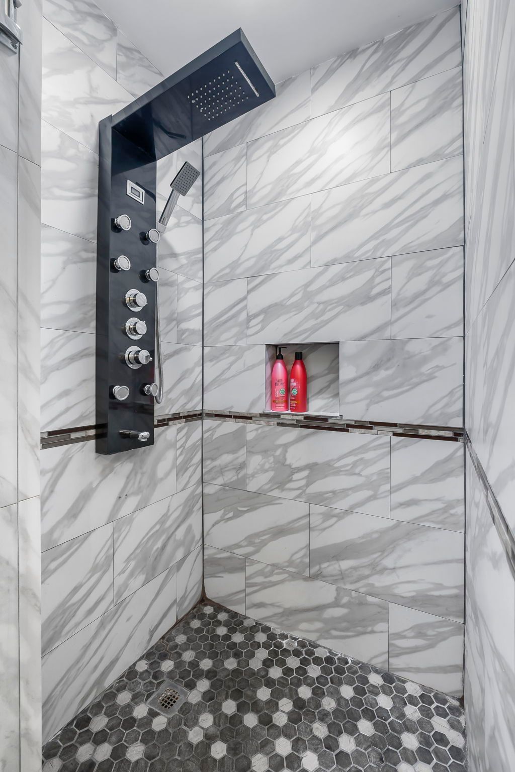 A shower with a black shower head and two bottles of shampoo on a shelf.