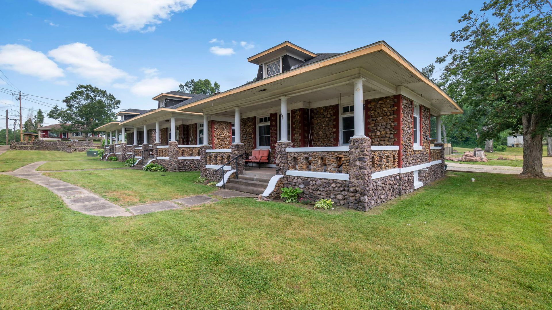 A large brick house with a large porch is sitting on top of a lush green field.