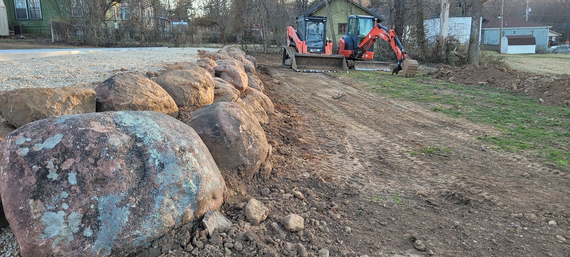 A large rock is sitting in the middle of a dirt road next to a bulldozer.