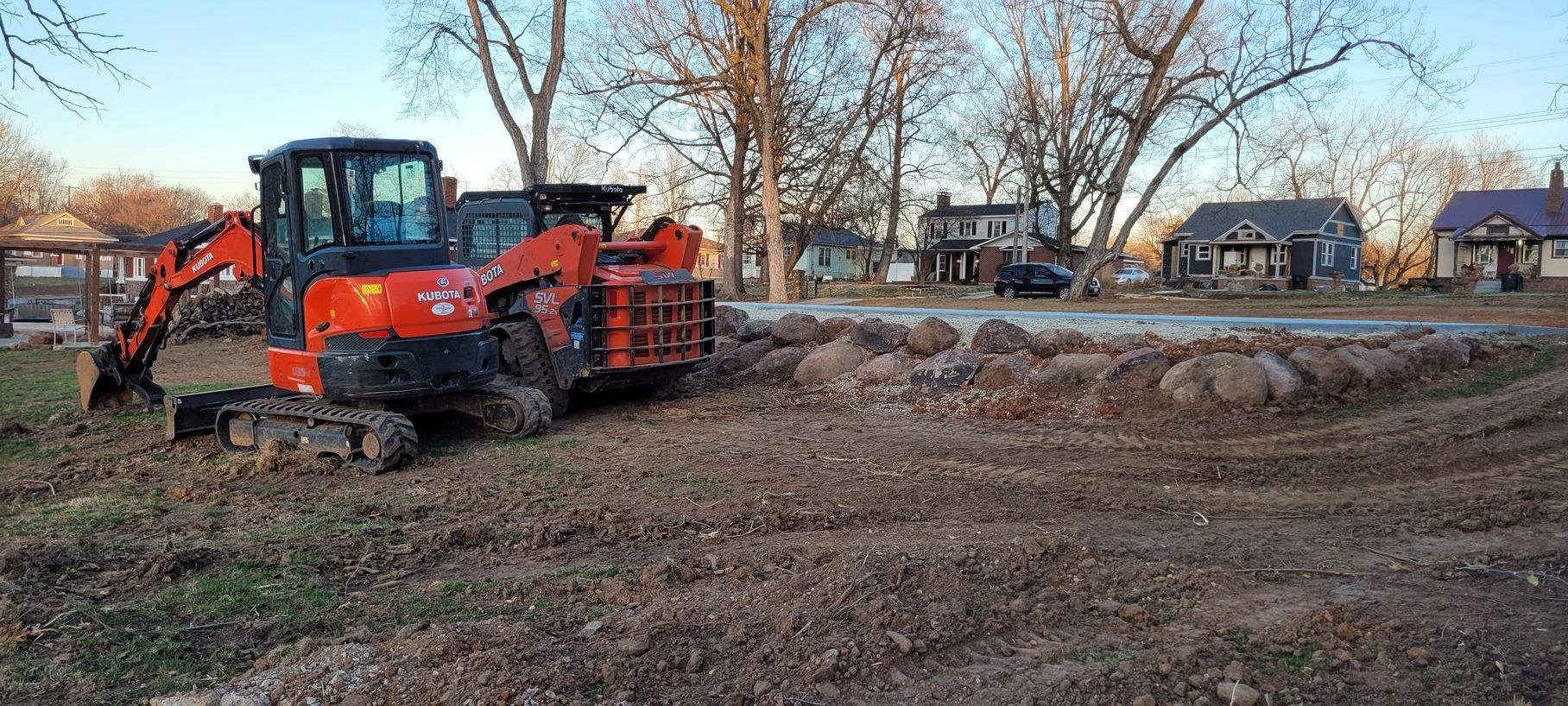 A red excavator is sitting in the middle of a dirt field.