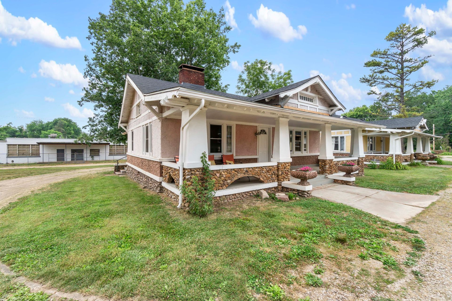 A house with a large porch is sitting on top of a lush green field.