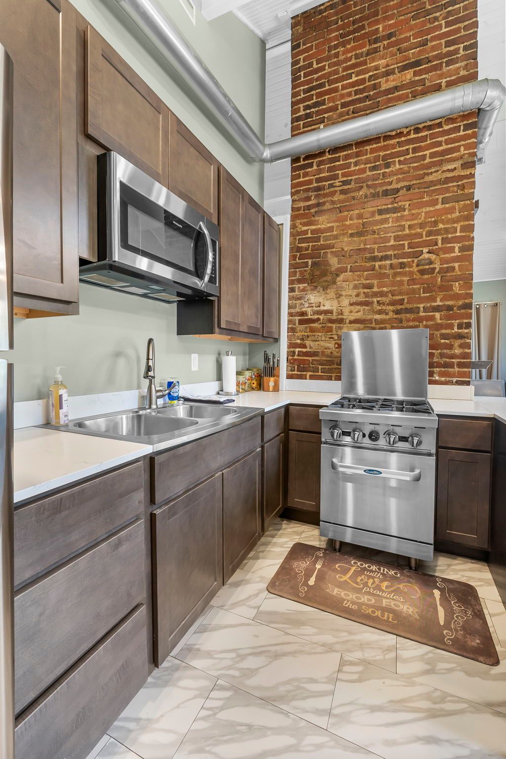 A kitchen with stainless steel appliances and a brick wall.