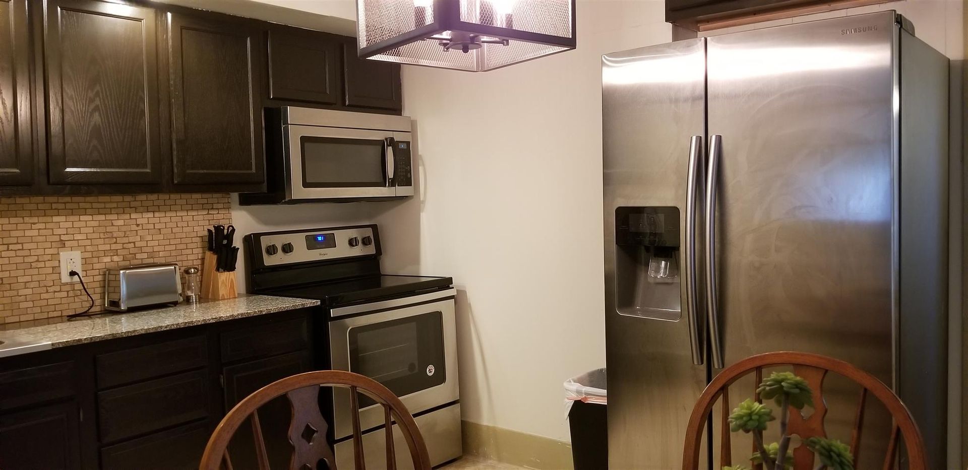 A kitchen with a stainless steel refrigerator , stove , microwave , and chairs.