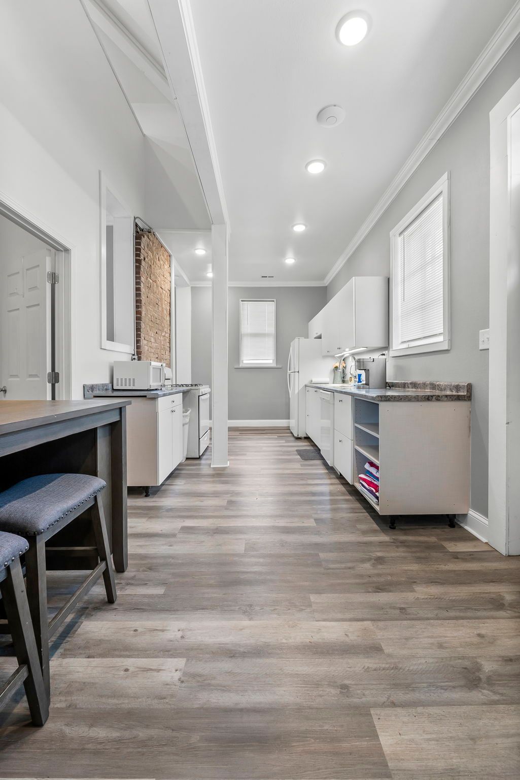 a long hallway leading to a kitchen with wooden floors and white cabinets .