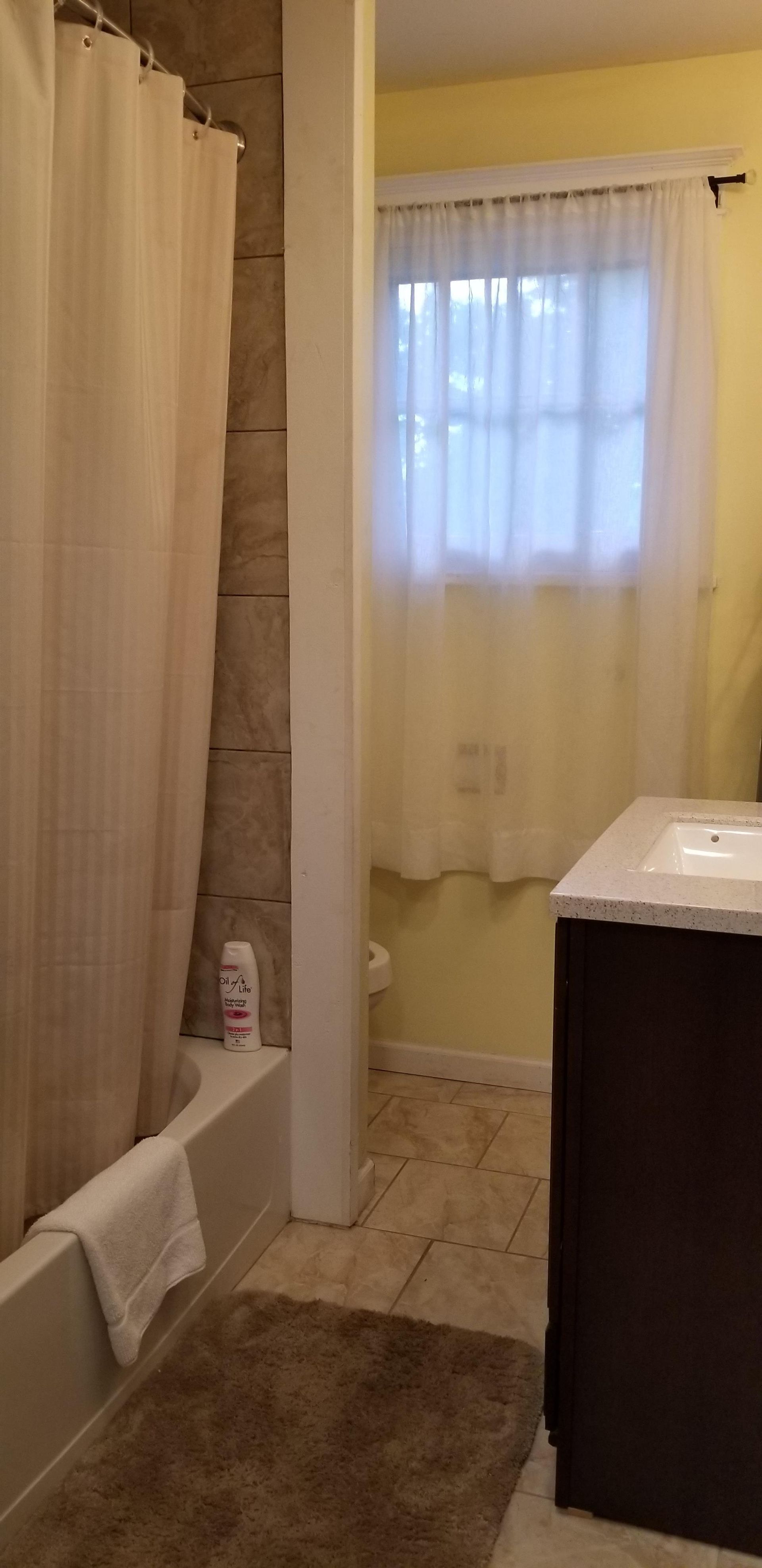 A bathroom with a tub , sink , window and shower curtain.