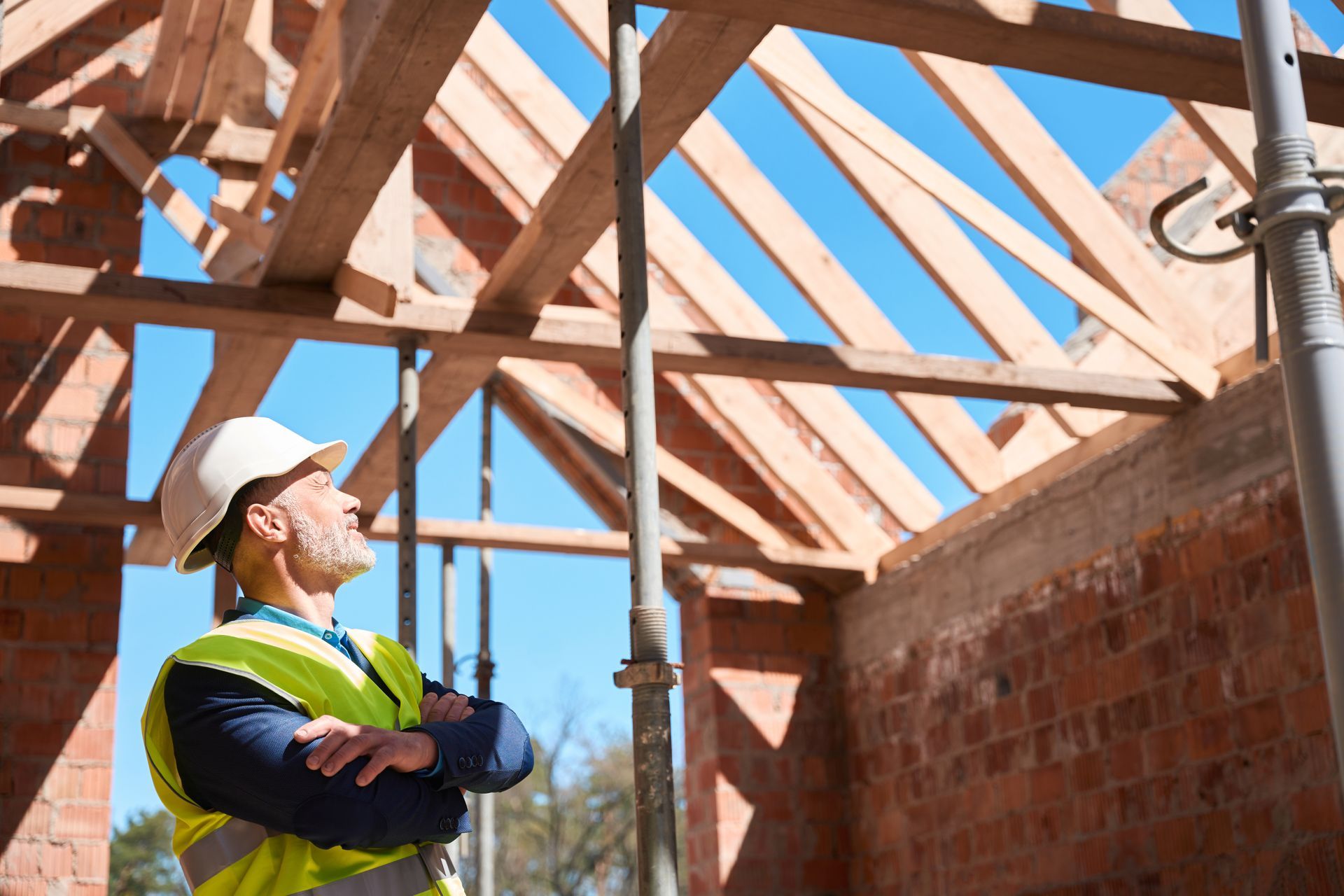 A construction worker is looking up at the roof of a building under construction.