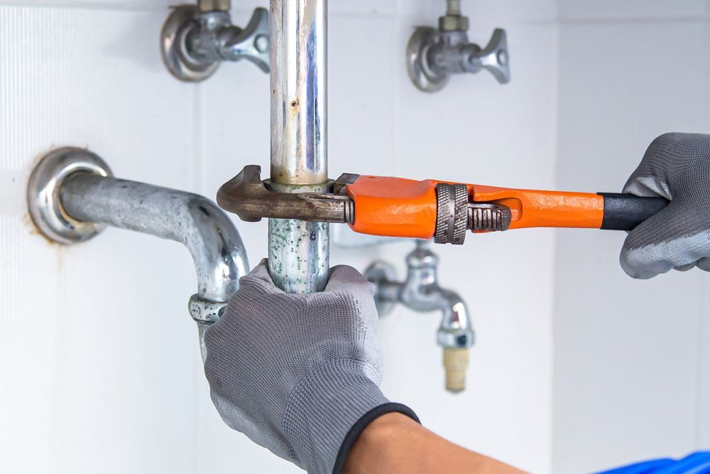 Plumber Using A Wrench To Repair A Water Pipe Under The Sink