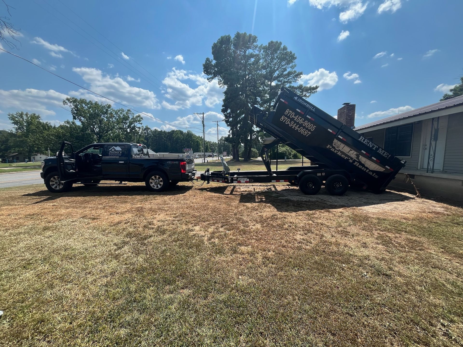 Blue dumpster with a black lid in a desert setting with mountains in the background.