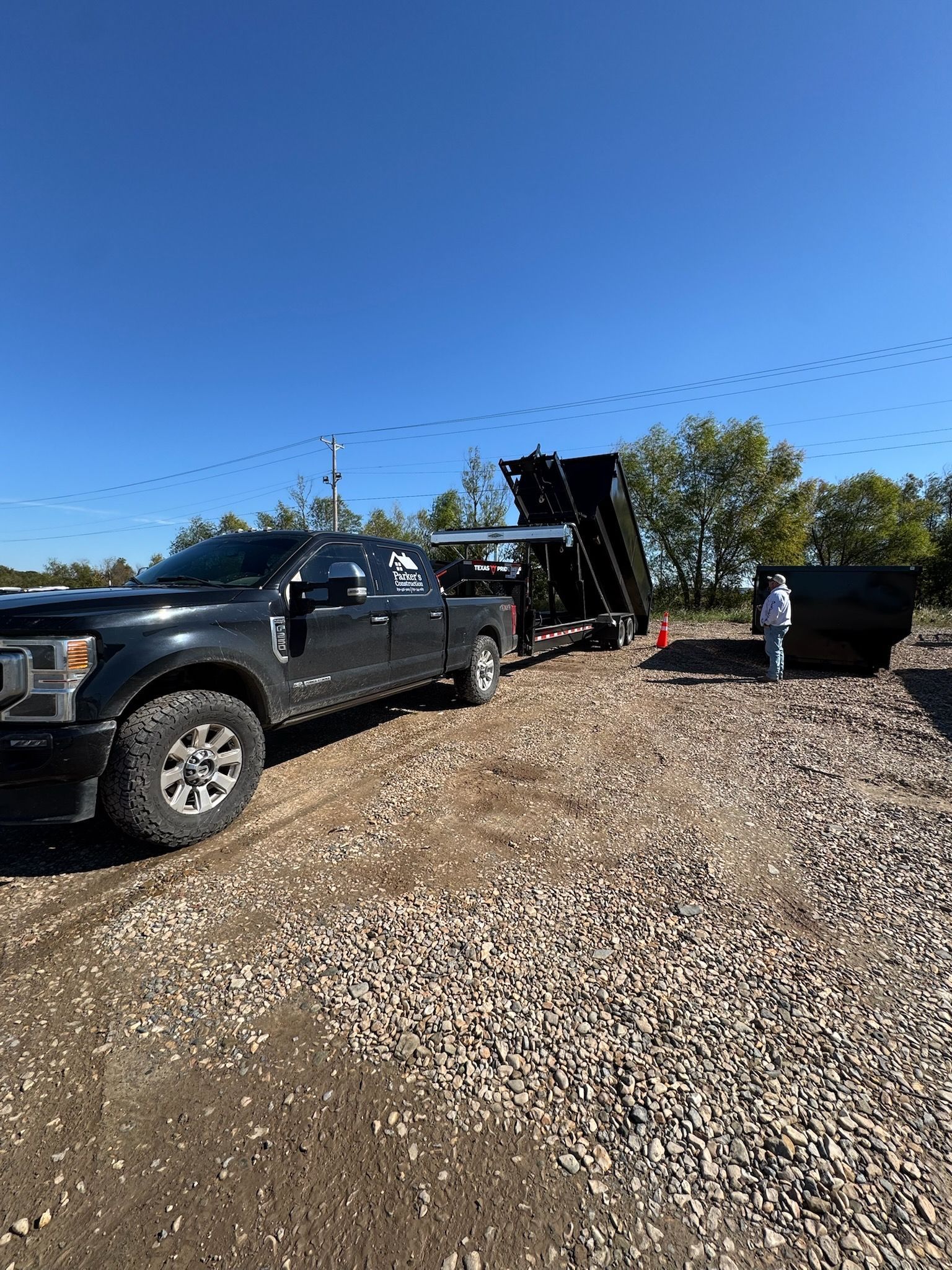 Two overflowing green dumpsters outdoors near a low fence, filled with trash.
