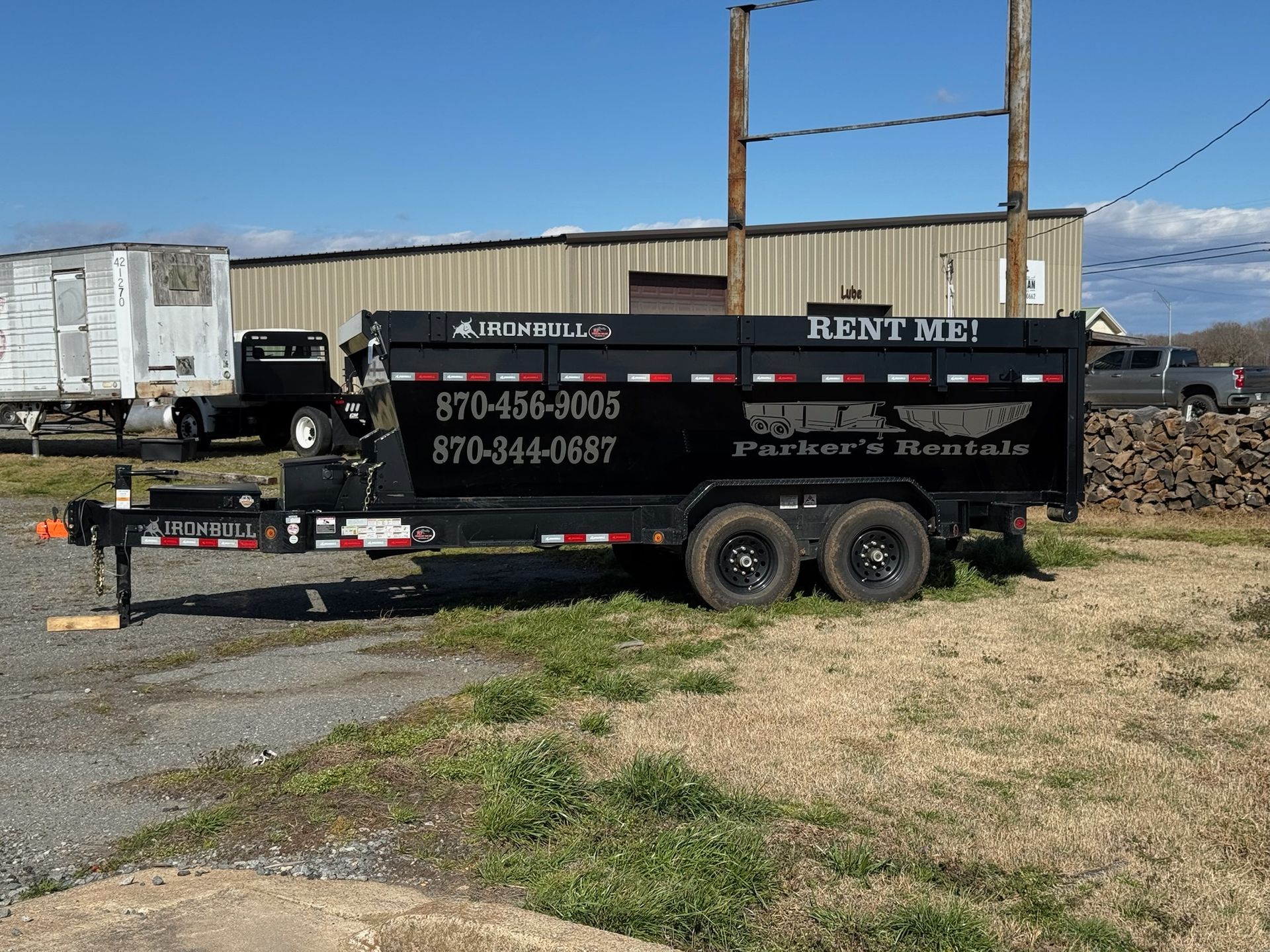 White dumpster next to a house under construction; sitting on reddish-brown dirt.