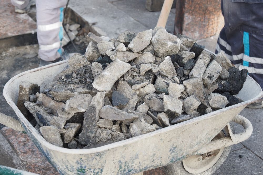 Wheelbarrow full of broken asphalt debris being shoveled, construction site.