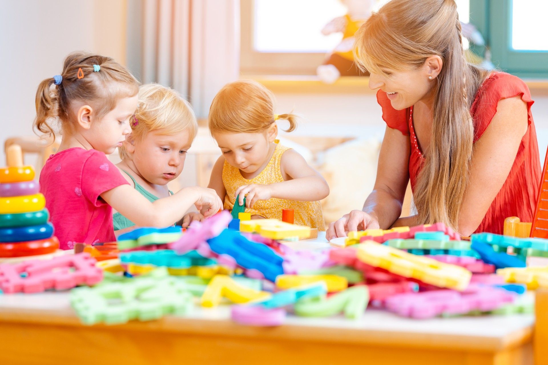 A woman and three children are playing with toys on a table.