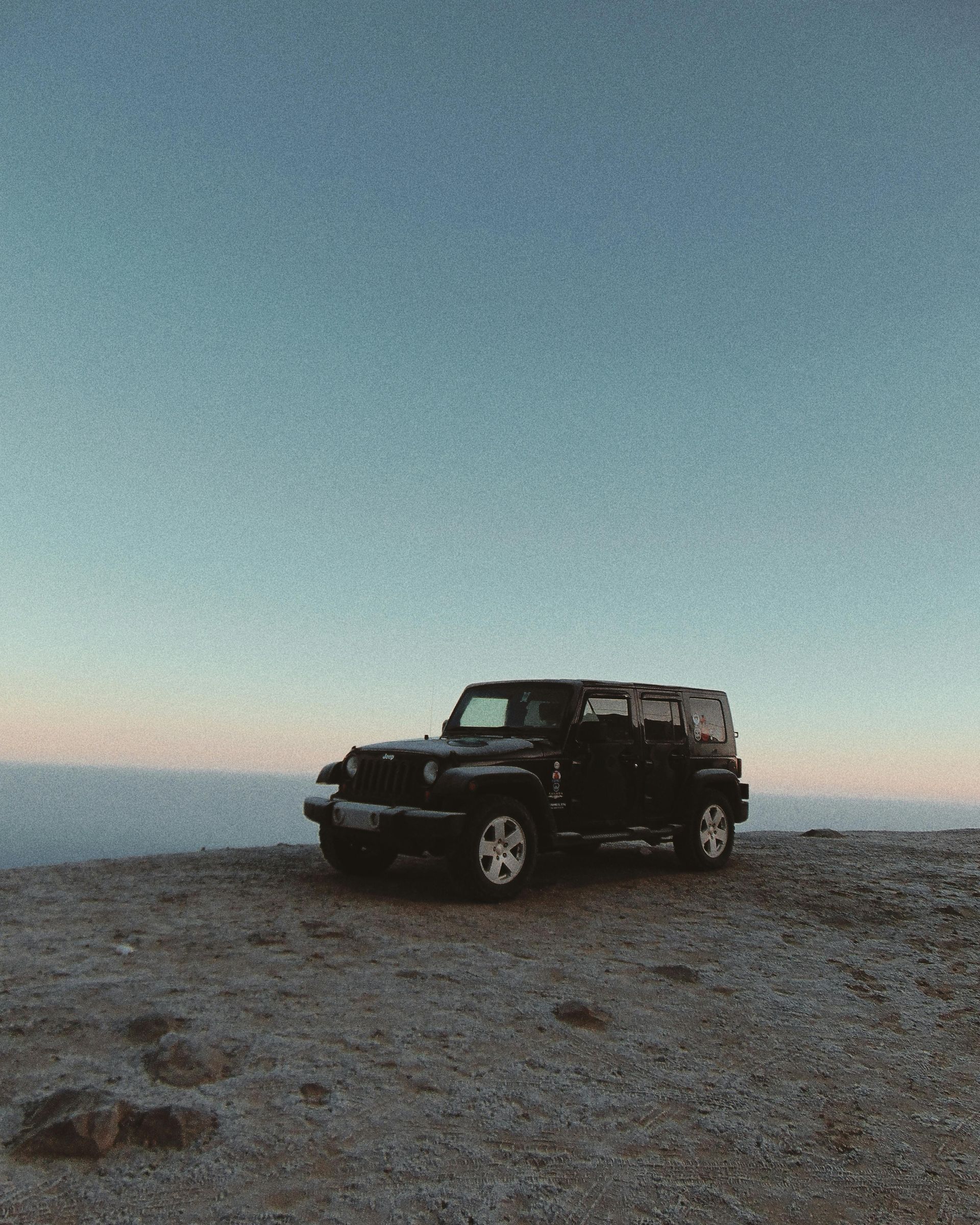 A black jeep is parked on top of a rocky hill.