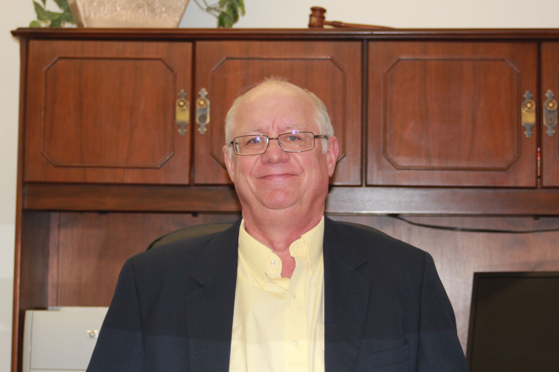 A man wearing glasses and a yellow shirt is standing in front of a wooden cabinet.