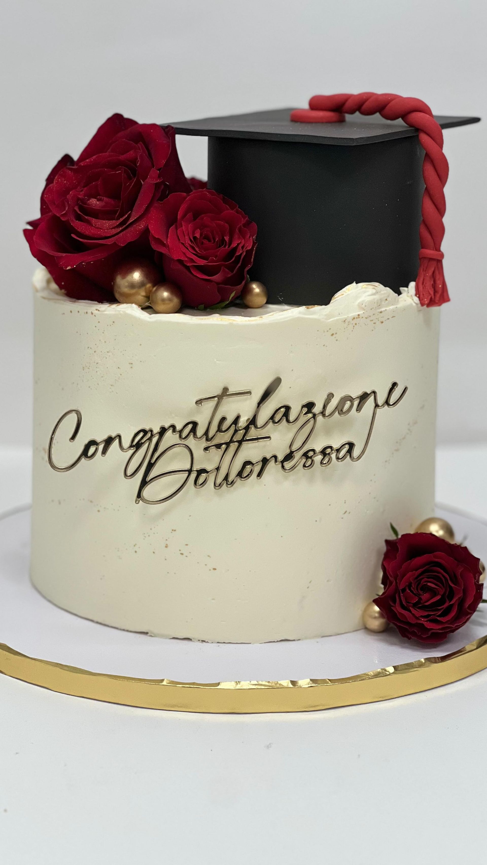 Torta di laurea con berretto nero, rose rosse, dettagli dorati e la scritta