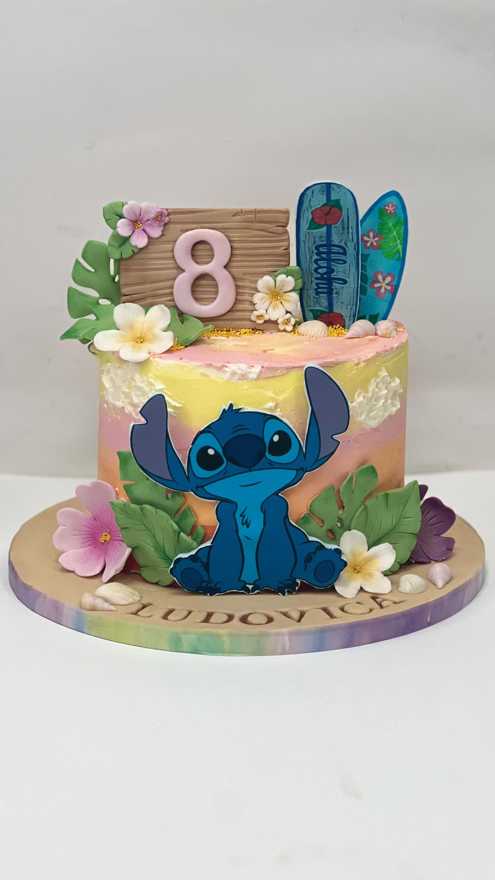 Torta di compleanno di Lilo e Stitch. Presenta Stitch, tavole da surf e il numero 8, con decorazioni floreali e tropicali.