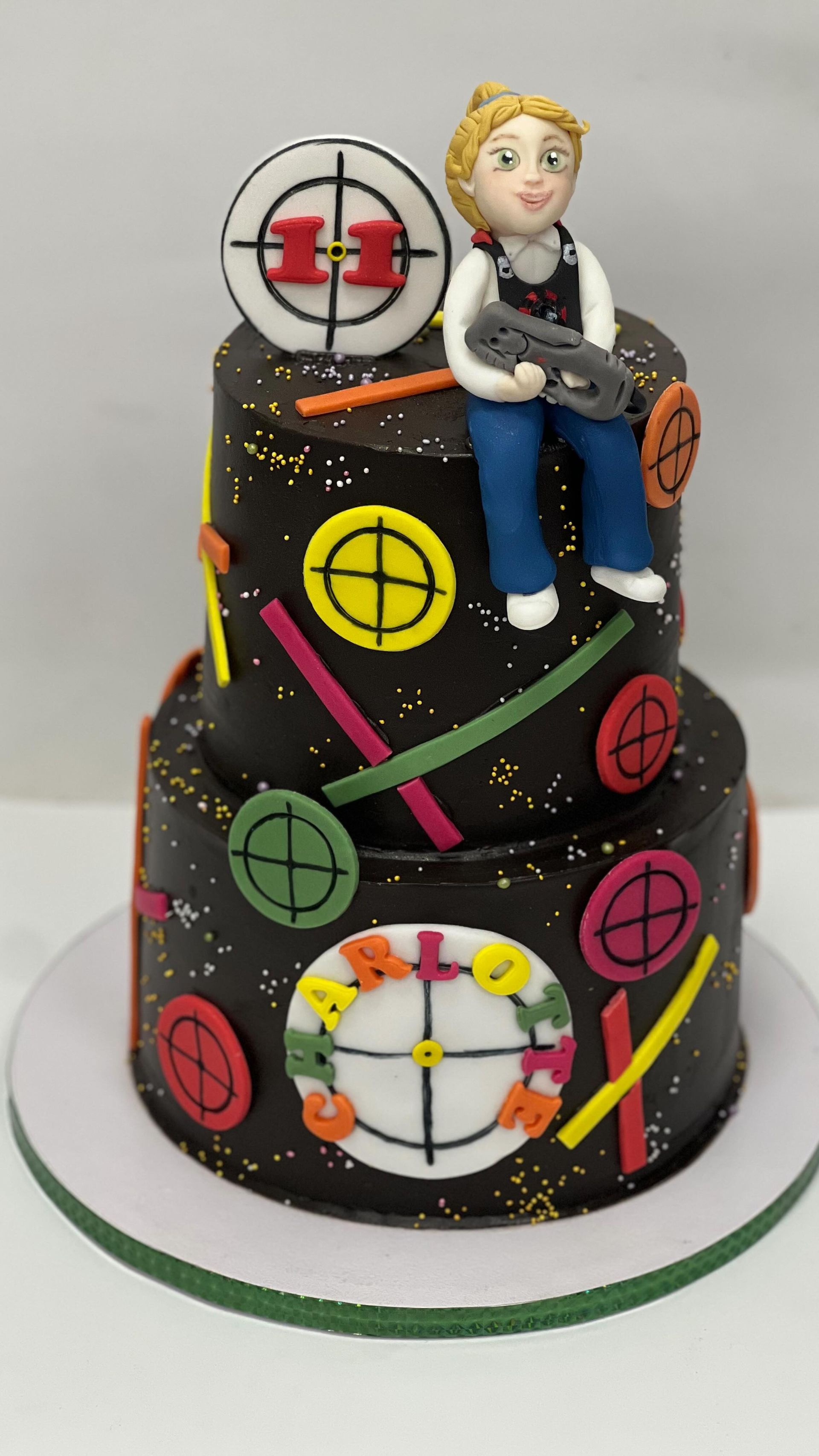 Torta a due piani decorata con bersagli e una figura di pasta di zucchero che impugna una pistola laser.