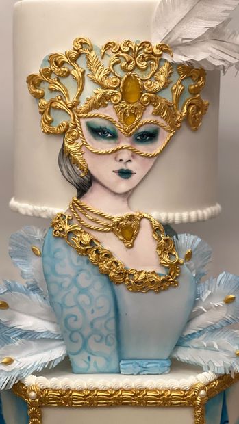 Torta in maschera con maschera dorata, piume e decorazioni blu e bianche.