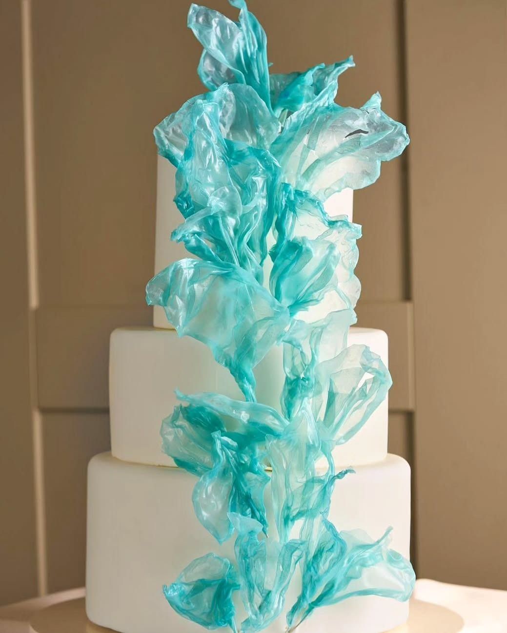 Torta nuziale bianca a tre piani con decorazioni in zucchero turchese che scendono lungo i lati.