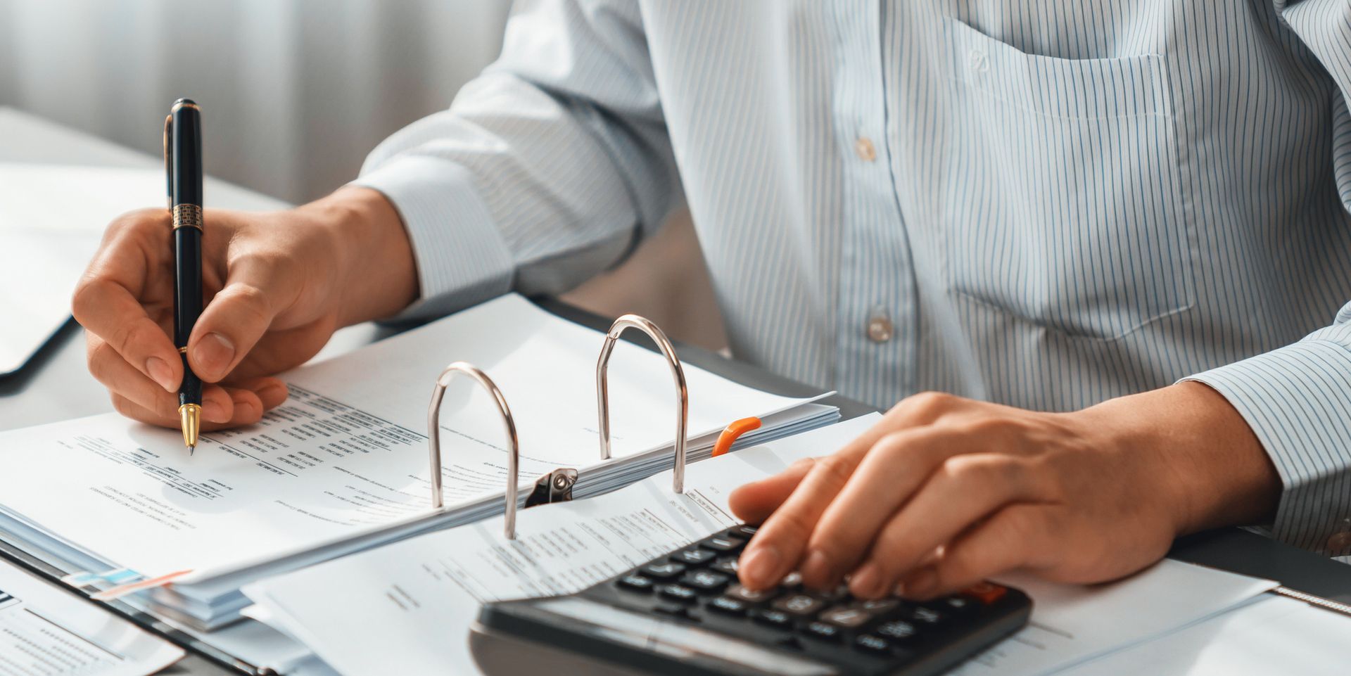 Corporate auditor calculating budget with calculator on his office desk.