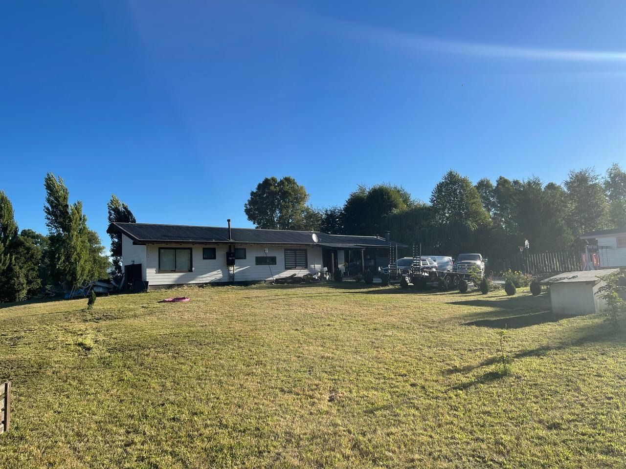 Una casa baja, blanca, con techo oscuro, se encuentra sobre una colina cubierta de hierba bajo un cielo azul brillante.
