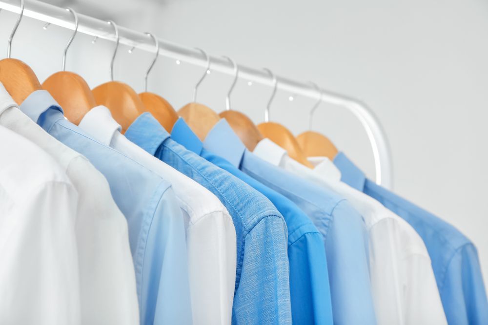 Row of White and Blue Dress Shirts Hanging on Wooden Hangers — Flynns Beach Service Laundry in Laurieton, NSW