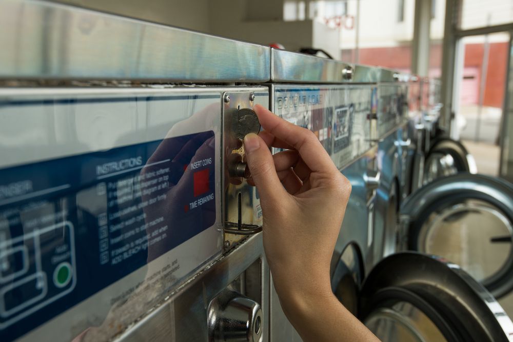 Hand Putting Coins in a Commercial Washing Machine — Flynns Beach Service Laundry in Port Macquarie, NSW