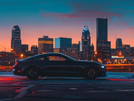 Black Mustang parked with city skyline at dusk.