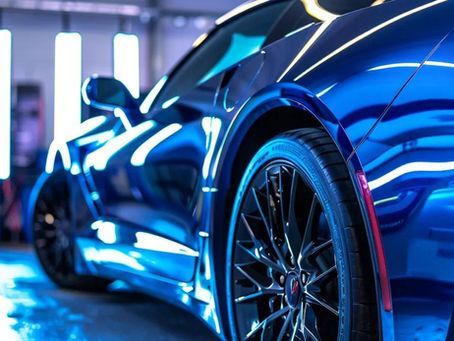 Blue sports car with shiny finish, reflective wheels, under blue light.