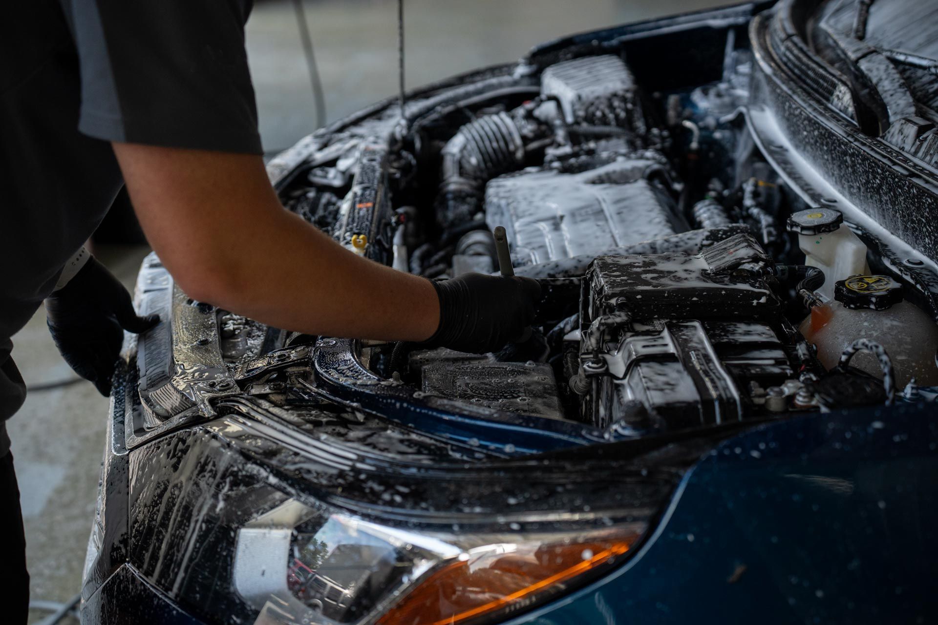 Person washing a car engine with foamy soap in a car wash setting.
