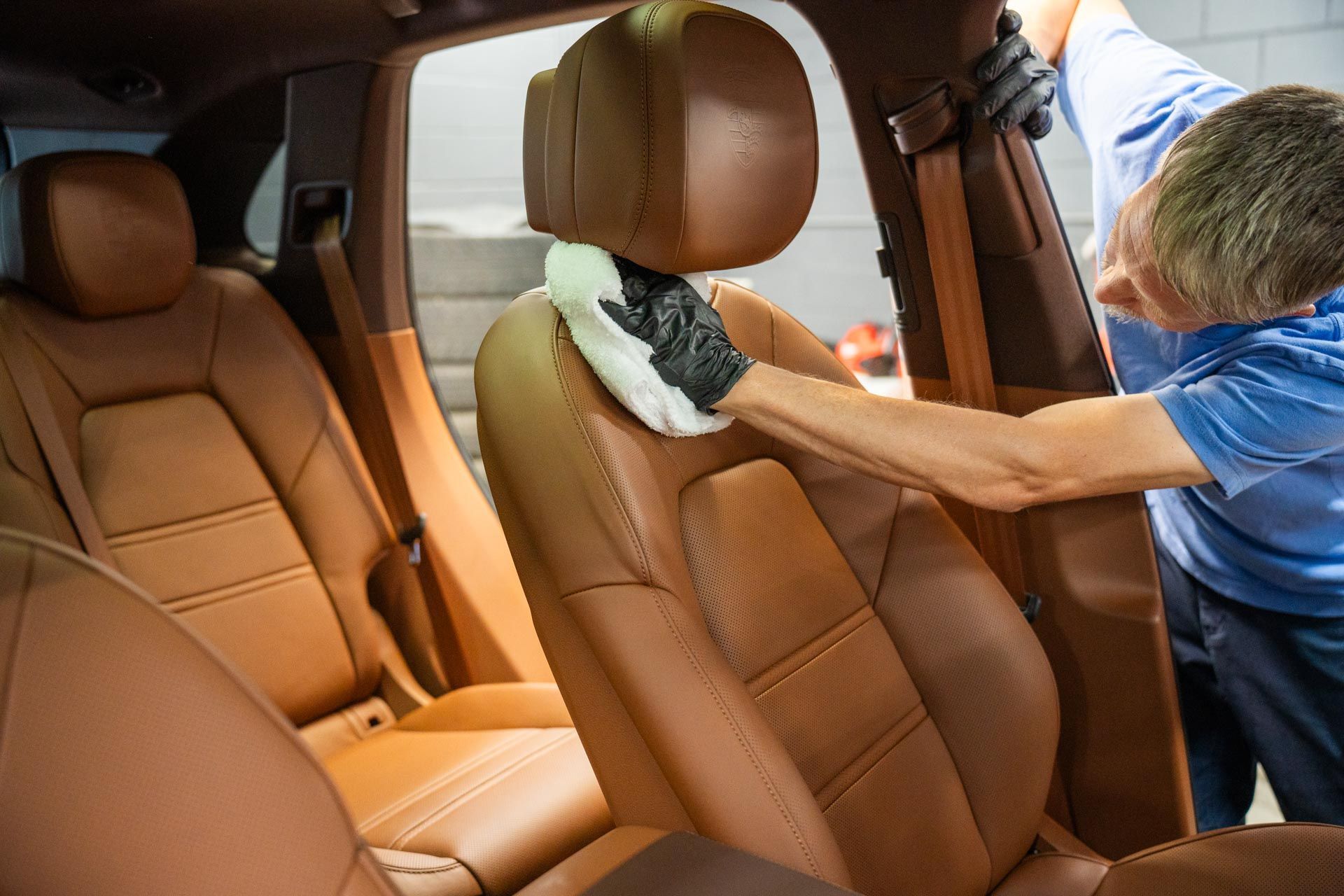 Person cleaning leather car seat with a white cloth and black gloves.