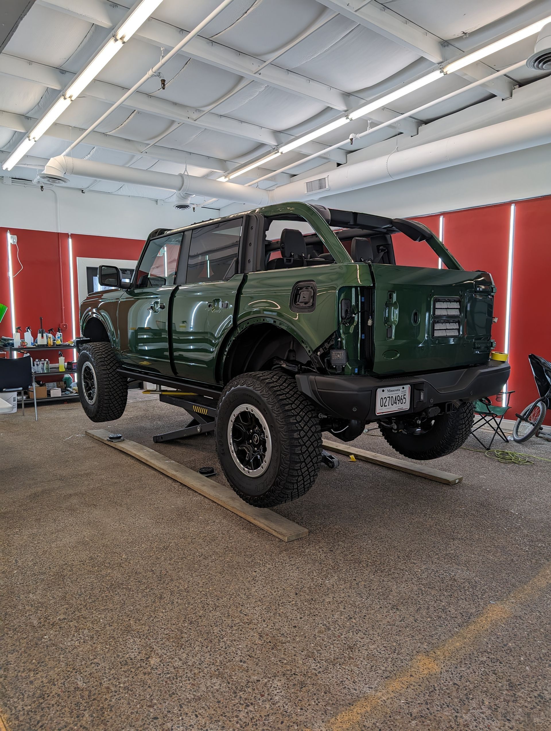 Green off-road SUV on a lift in a garage, with the top removed.