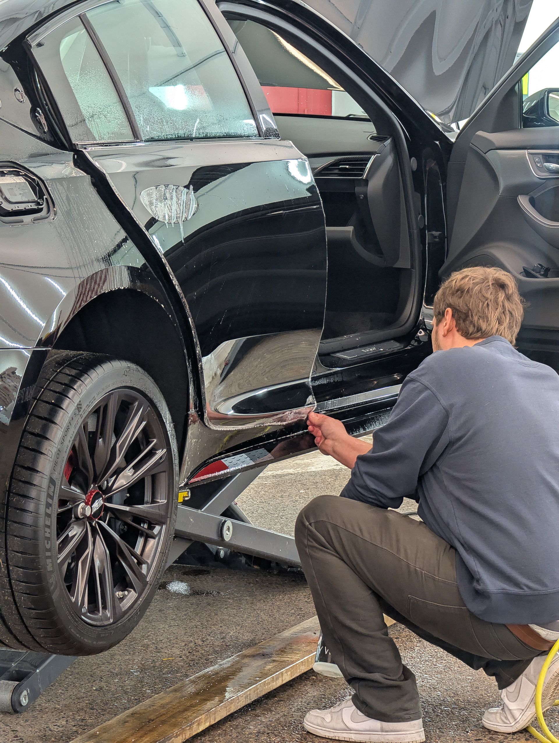 Man cleaning a black car's door sill. Car is on a lift.