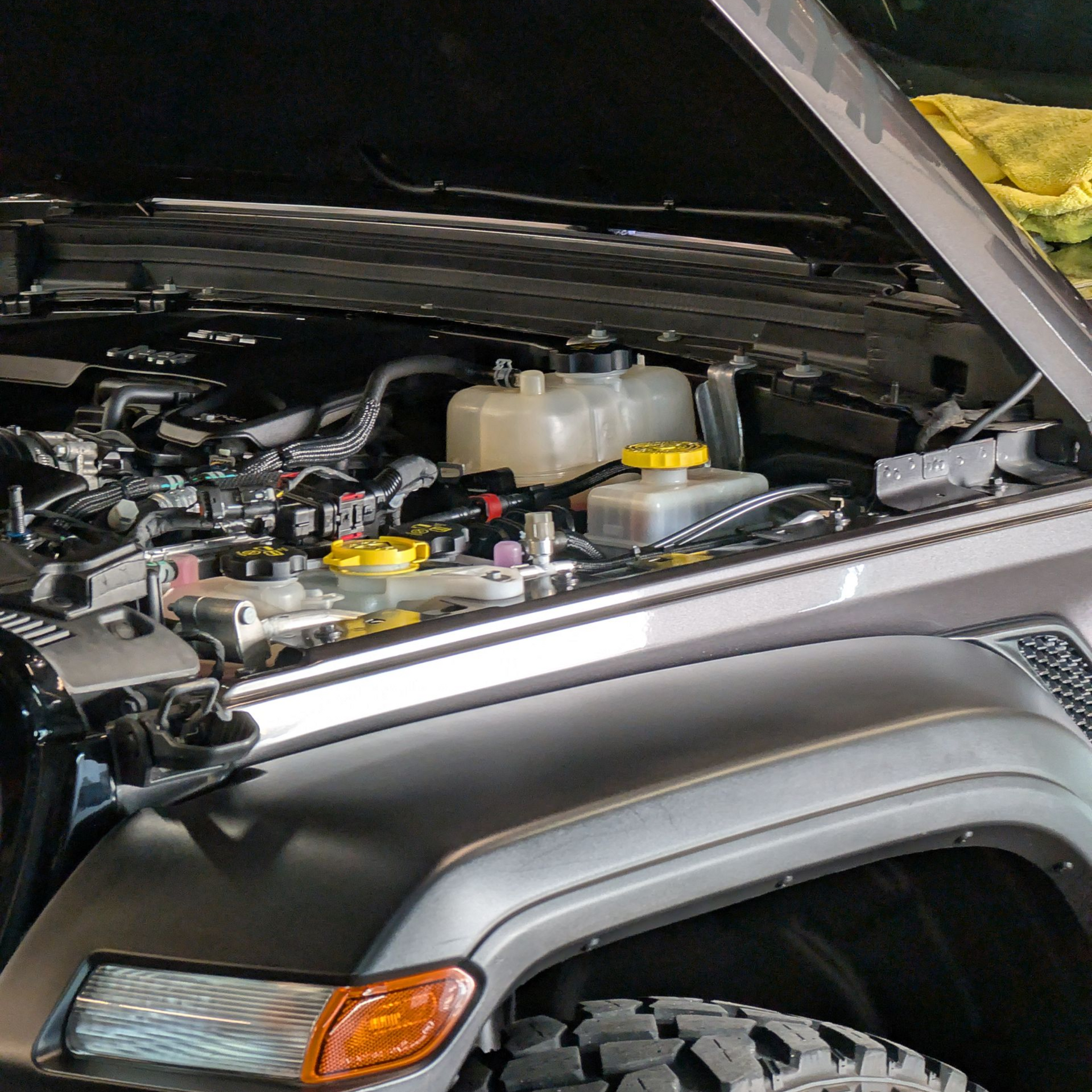 Open car hood revealing engine components, featuring coolant reservoirs and yellow caps.