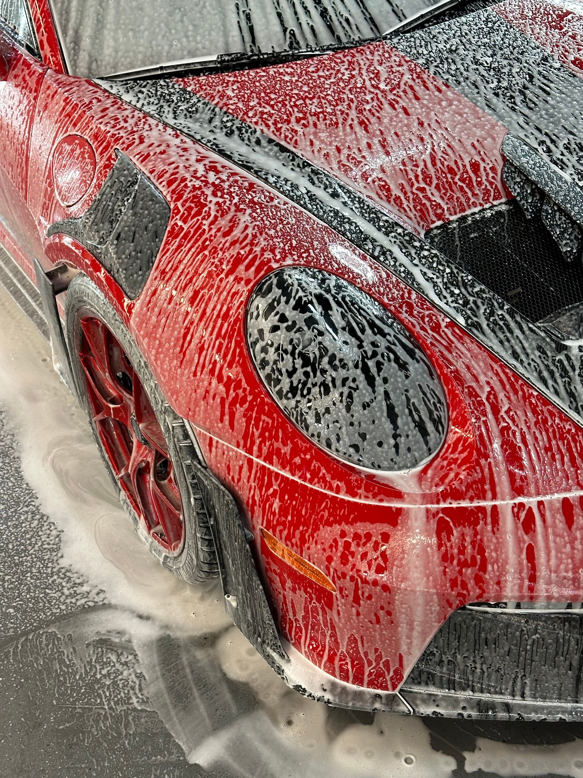 Person wearing black gloves wiping a blue car with an orange cloth.