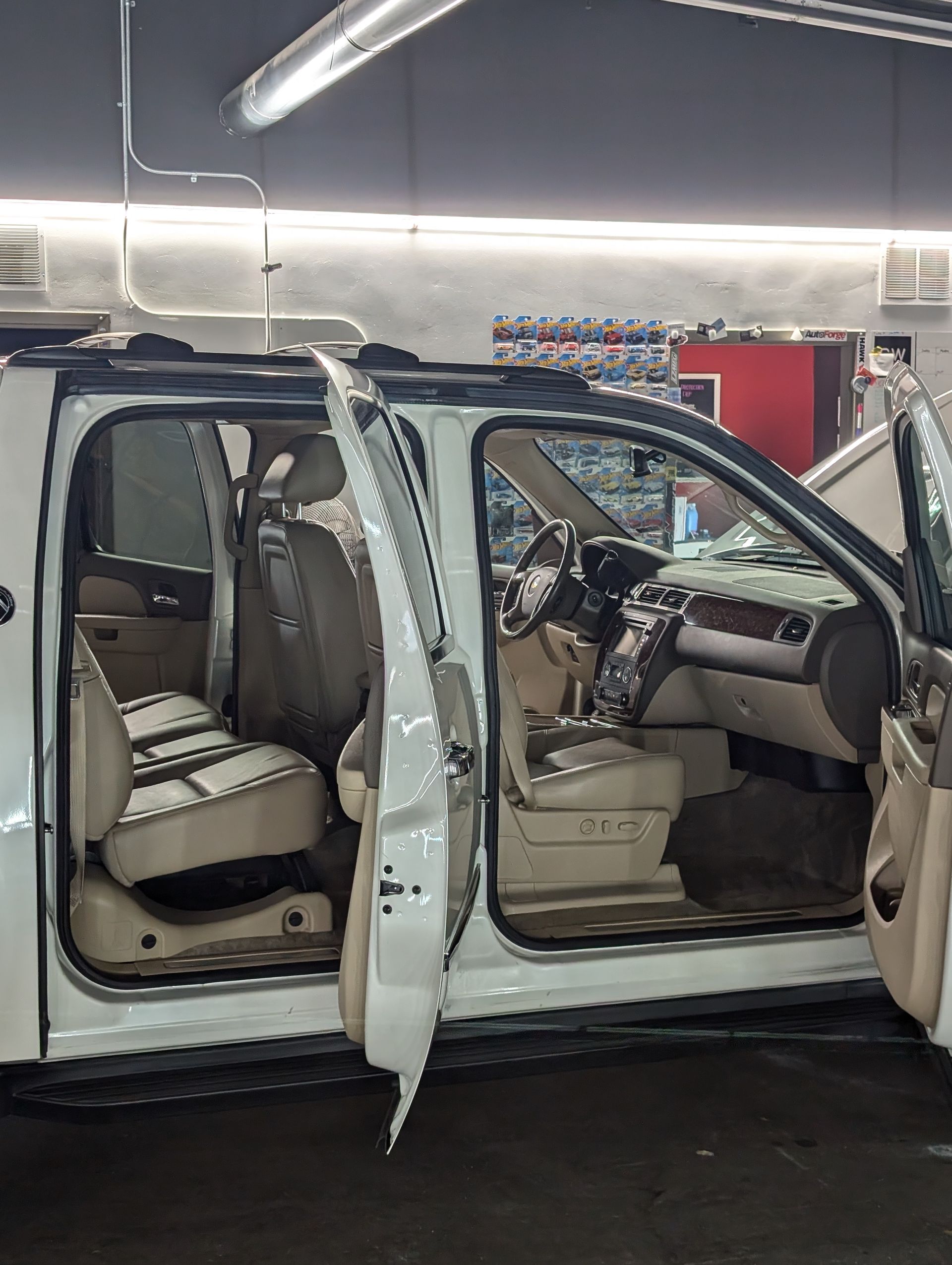 White SUV with doors open, interior visible. Beige leather seats and dashboard. Garage setting.