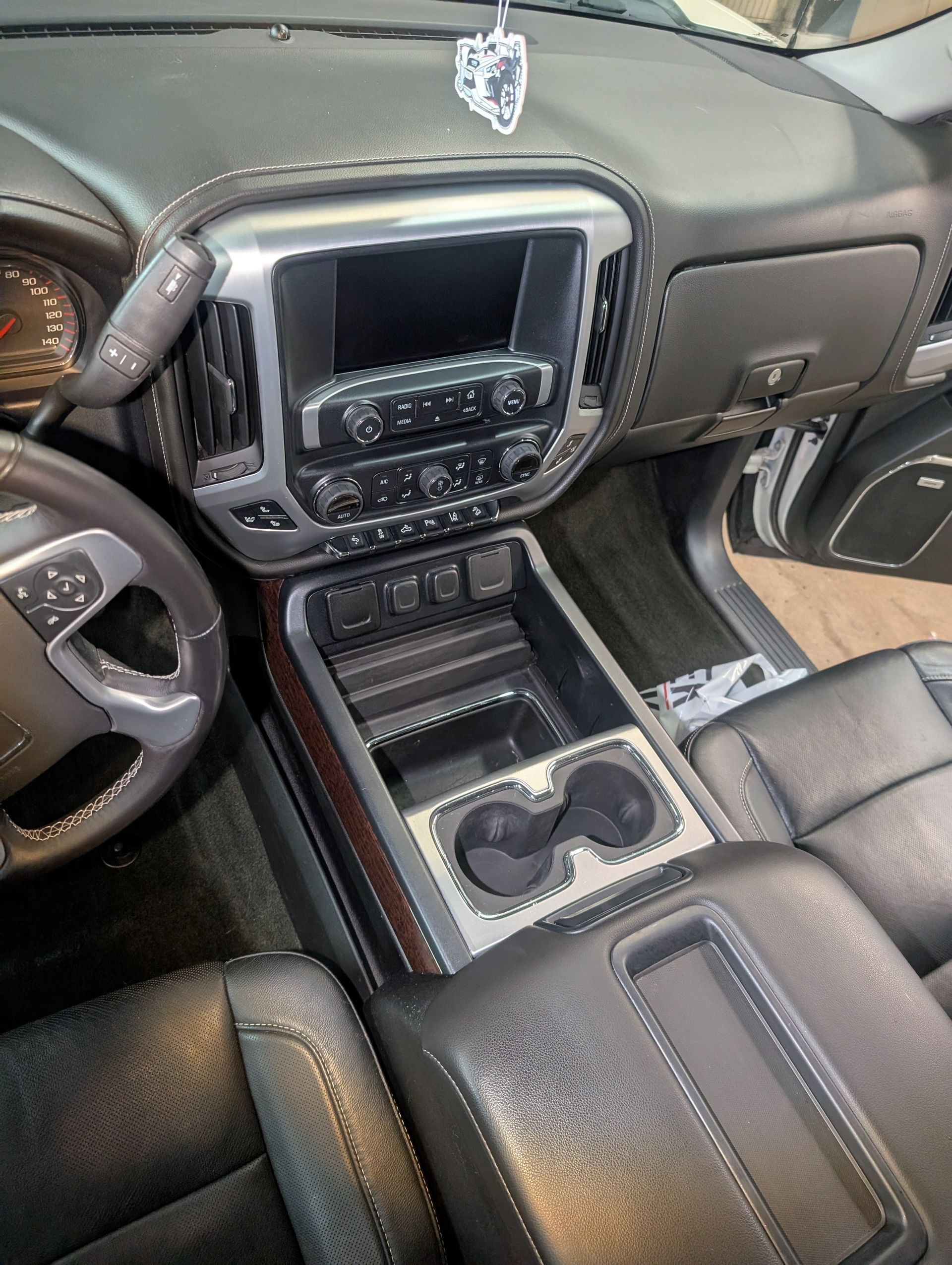 Black and silver car dashboard, including a touchscreen, cup holders, and steering wheel.