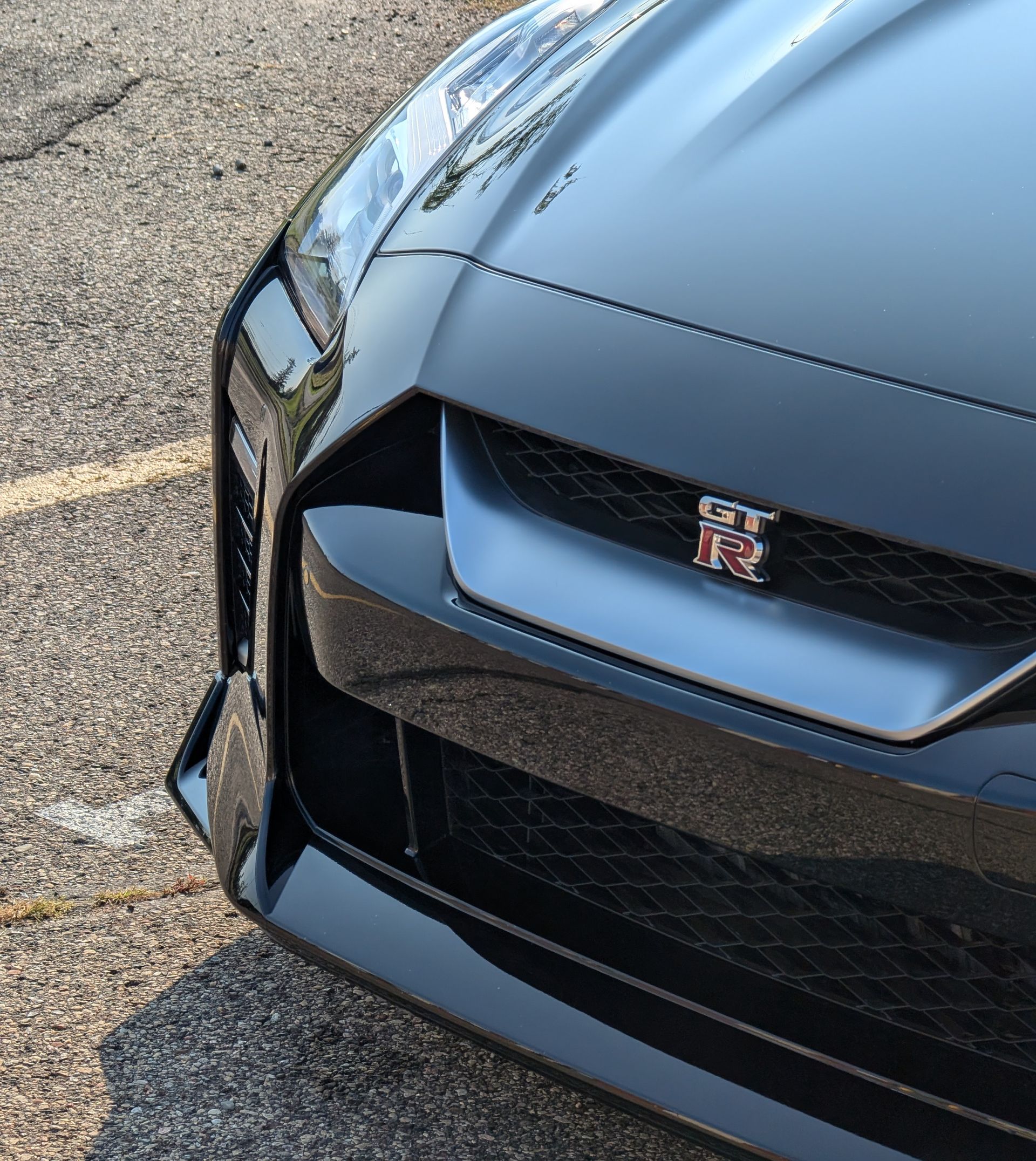 Close-up of a black Nissan GT-R sports car front end; silver grill and red GT-R emblem.