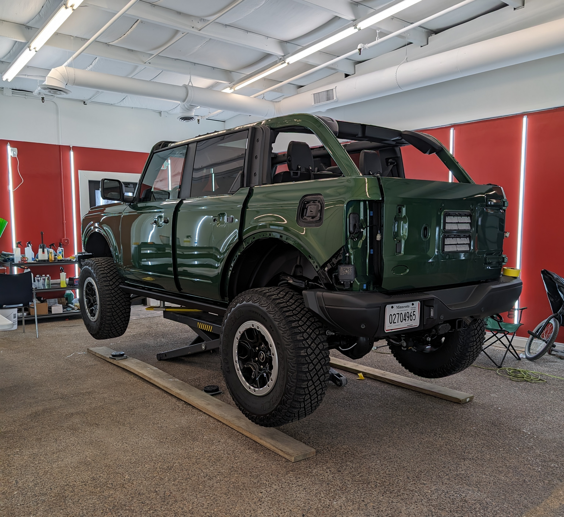 Green SUV on a lift in a garage. Back section of the vehicle is detached.