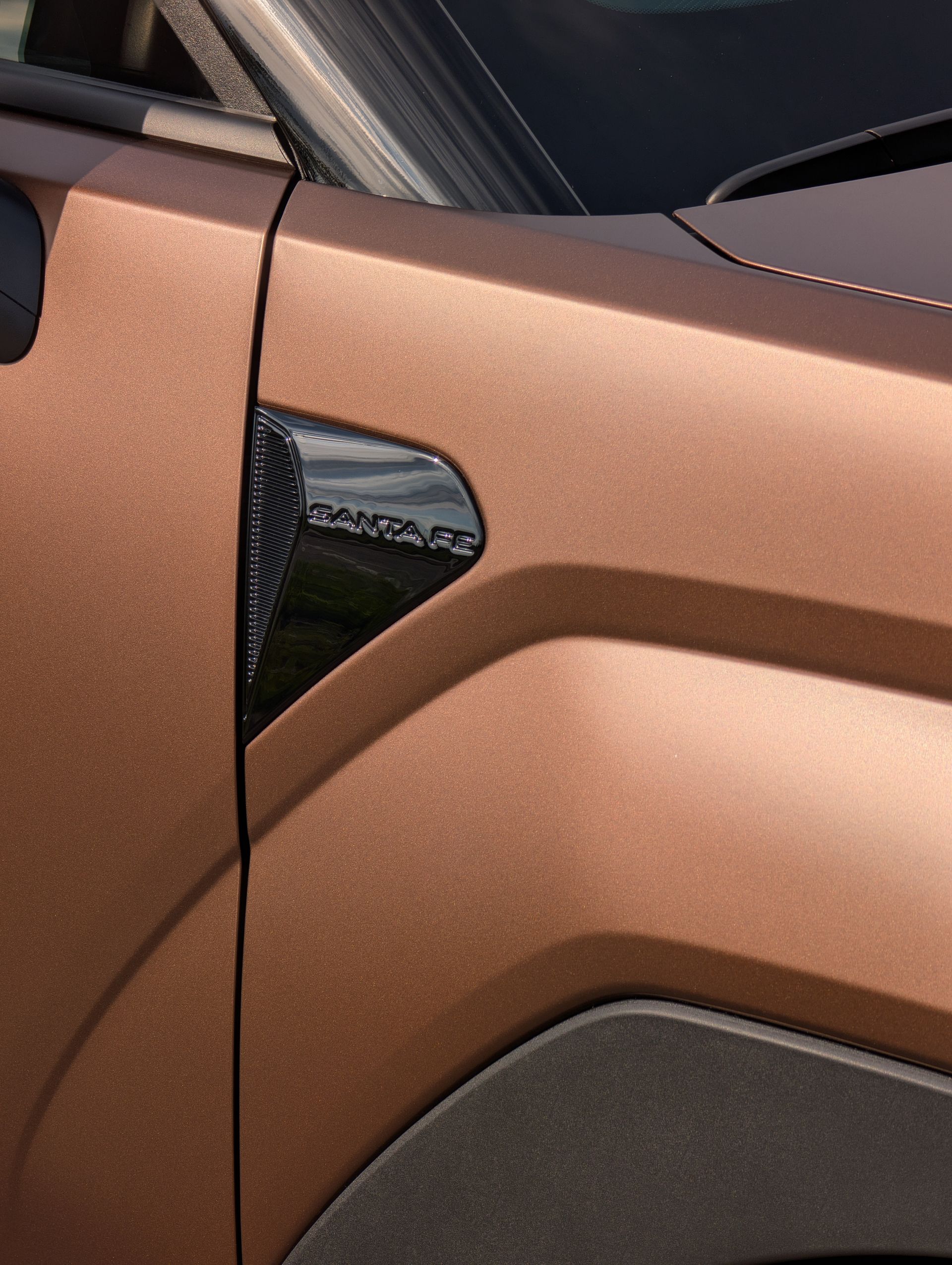 Bronze car fender detail with black trim and a vent.