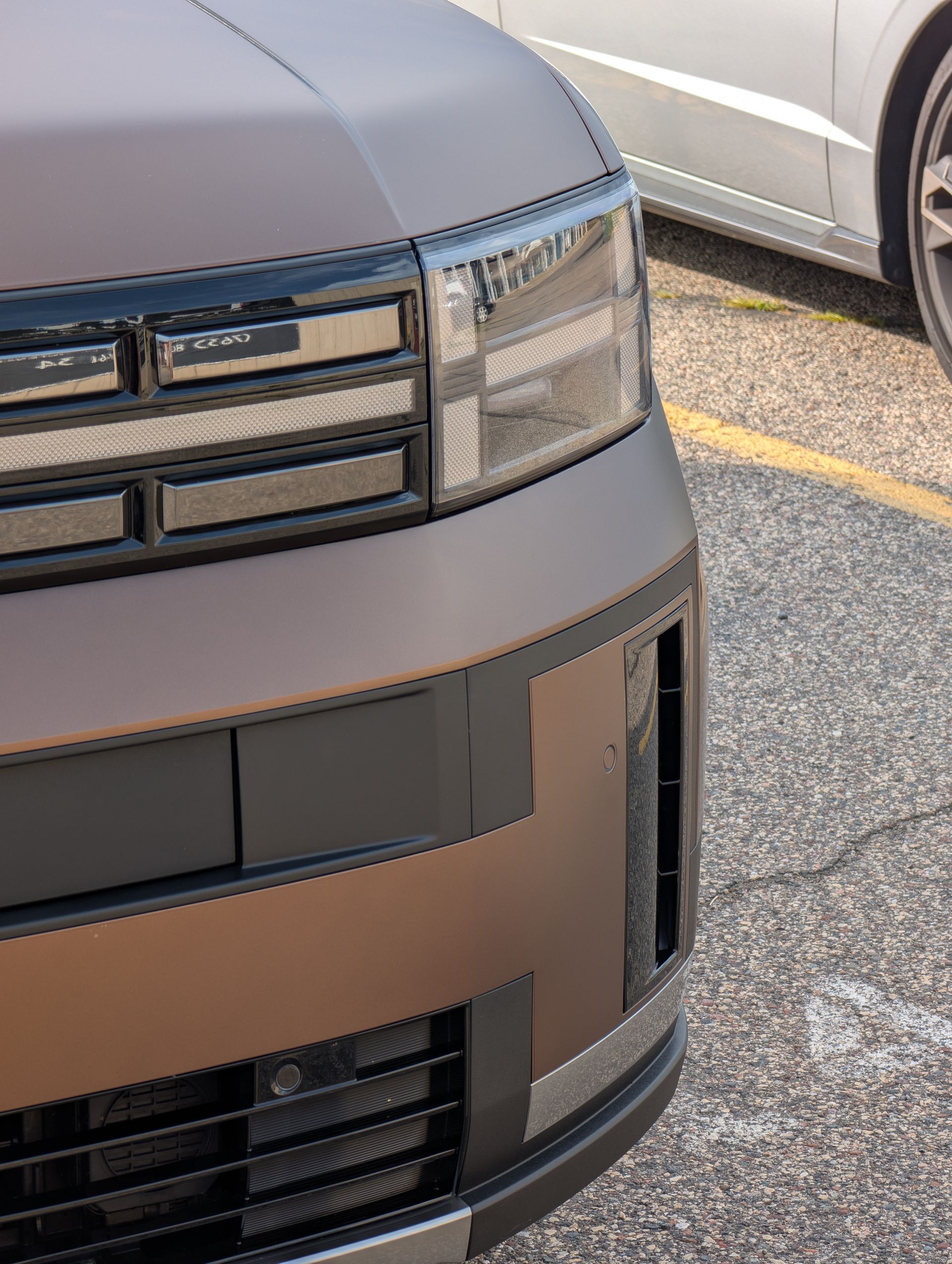 Close-up of a brown car front. Rectangular headlights, black grill, and a black bumper.