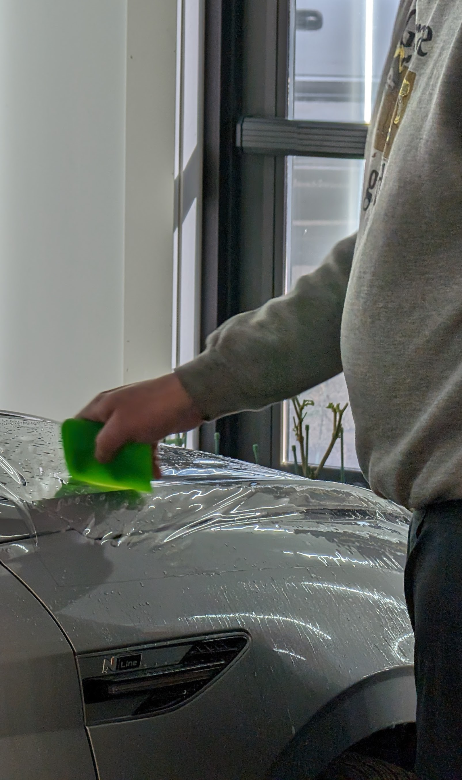 Person applying protective film to a blue car's headlight area.