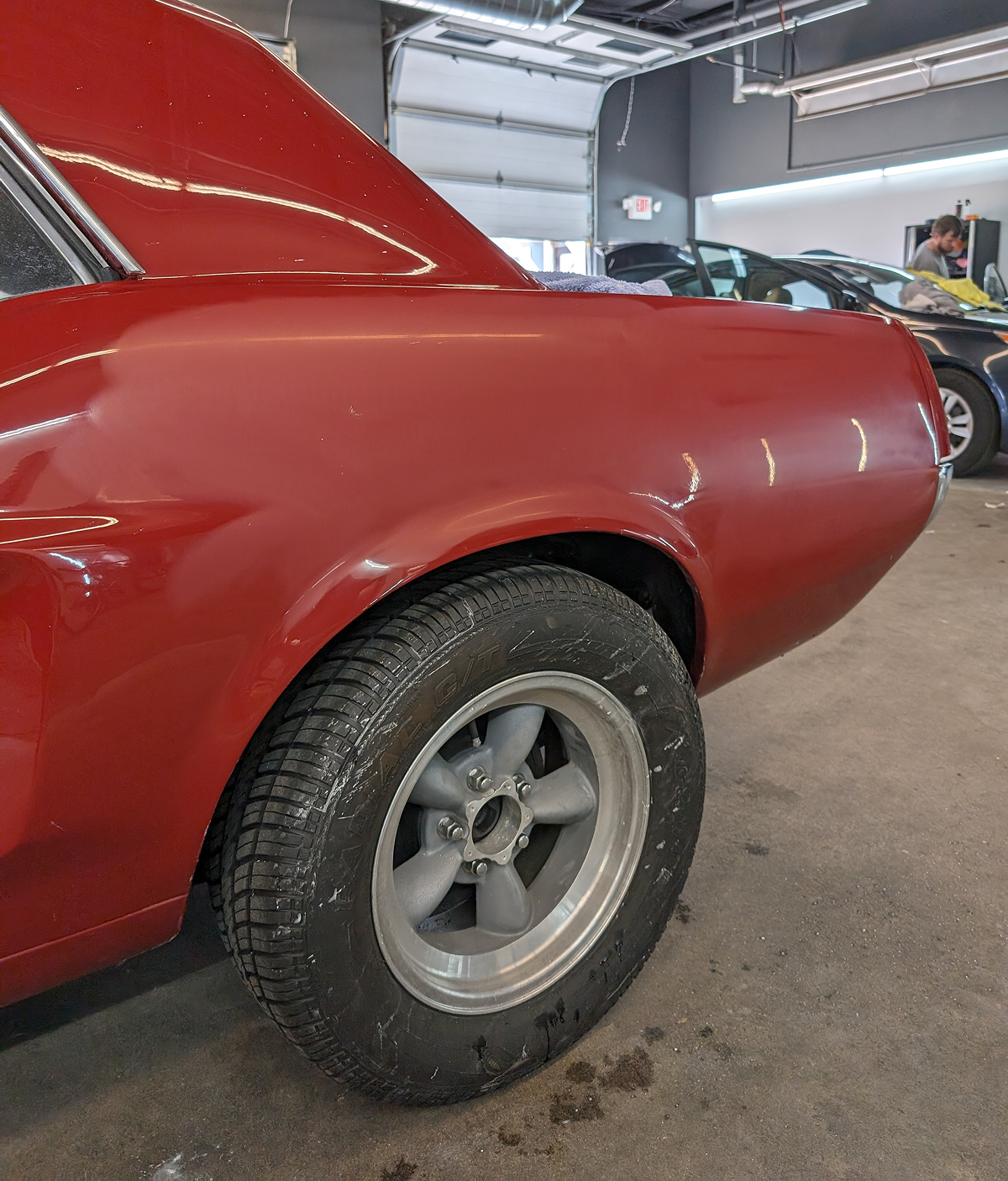 Red classic car's rear quarter panel and tire; silver wheel, inside a garage.