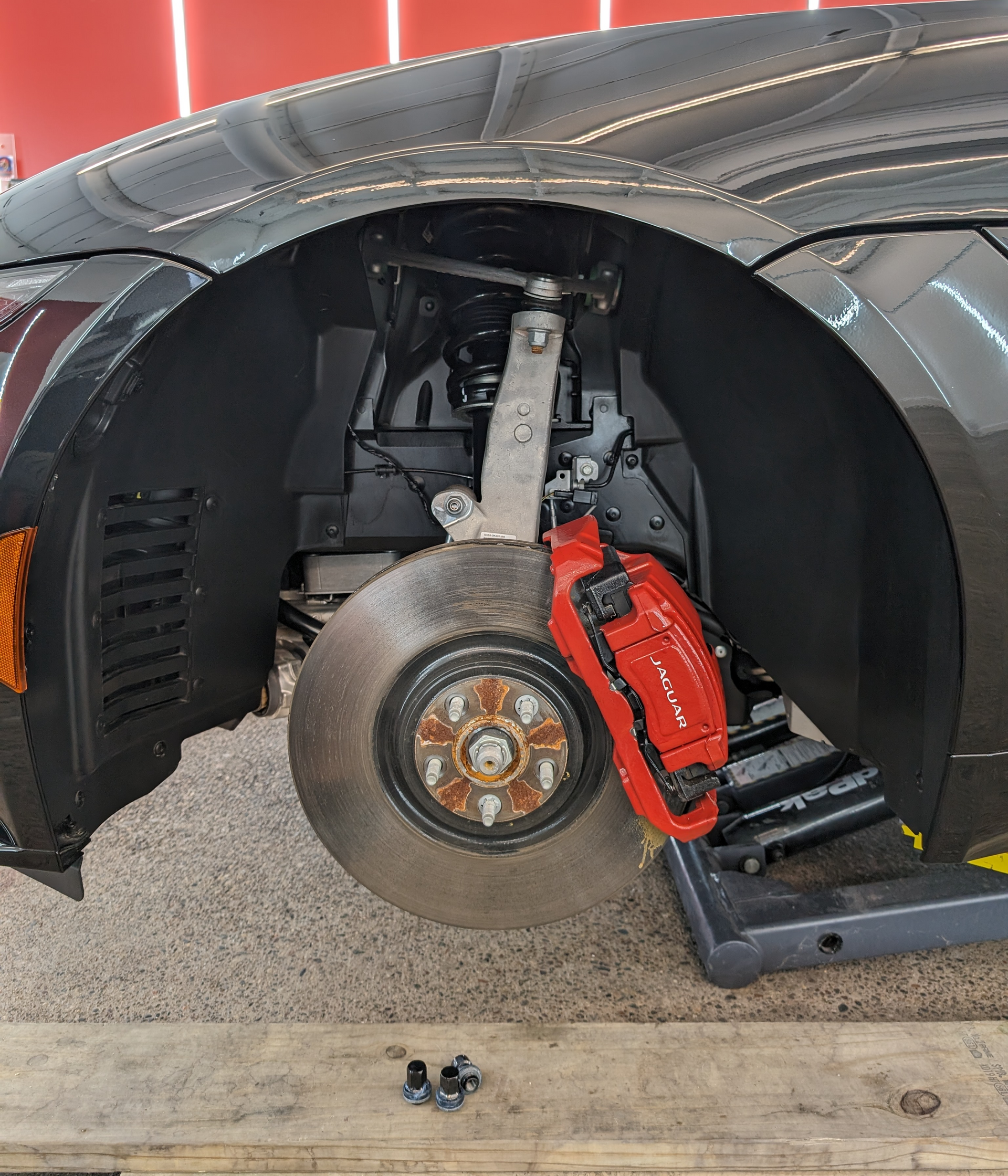 Car wheel well with red brake caliper, rotor, and suspension components visible.