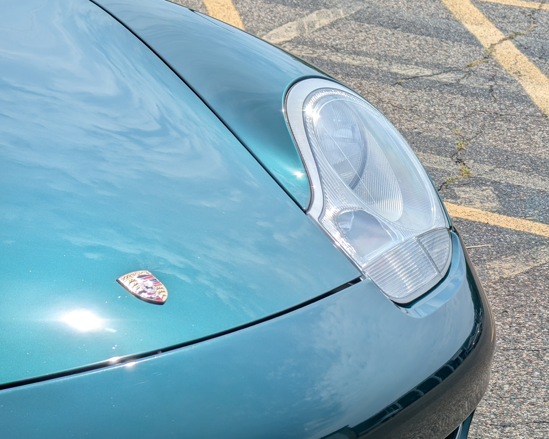 Teal Porsche sports car hood and headlight, with Porsche emblem visible.